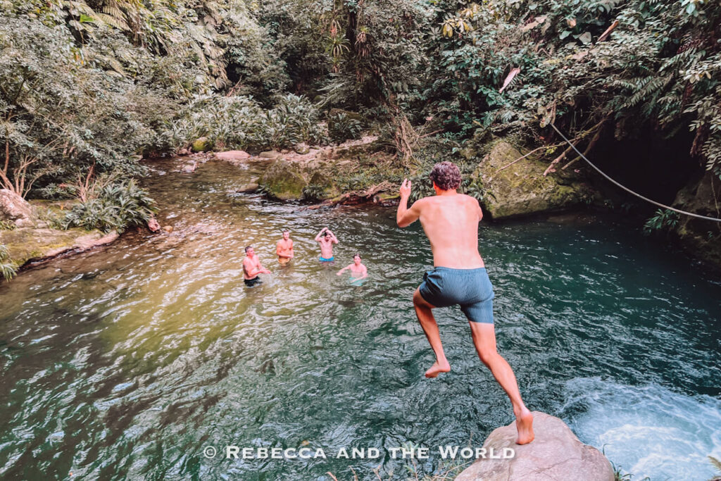 Traveler jumping into a jungle swimming hole while others watch from the water during the Ciudad Perdida hike.