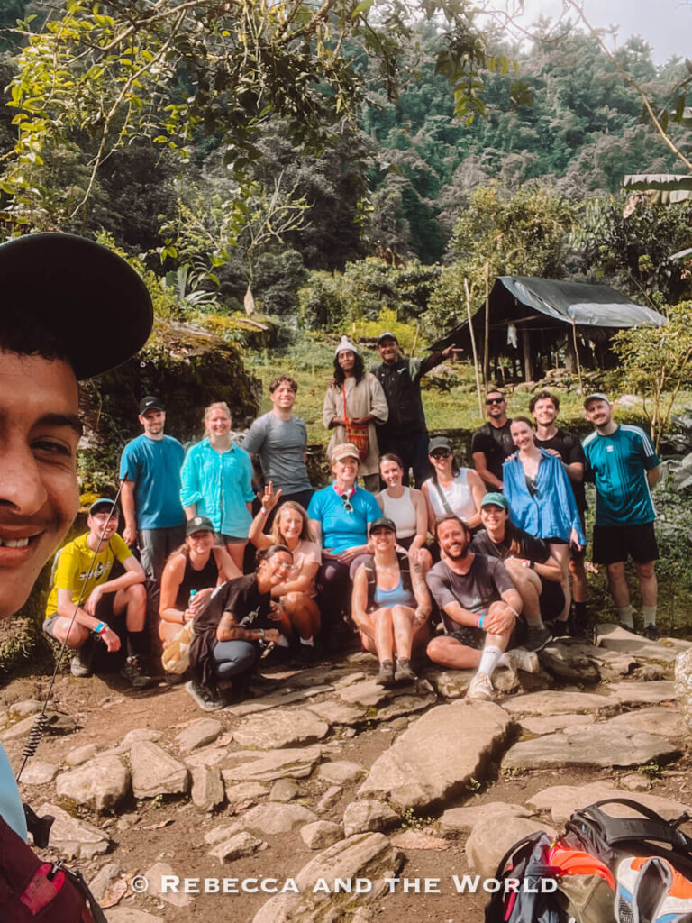 Large group photo of trekkers, guides, and an Indigenous Kogi person during the Lost City trek in a jungle village near Ciudad Perdida.