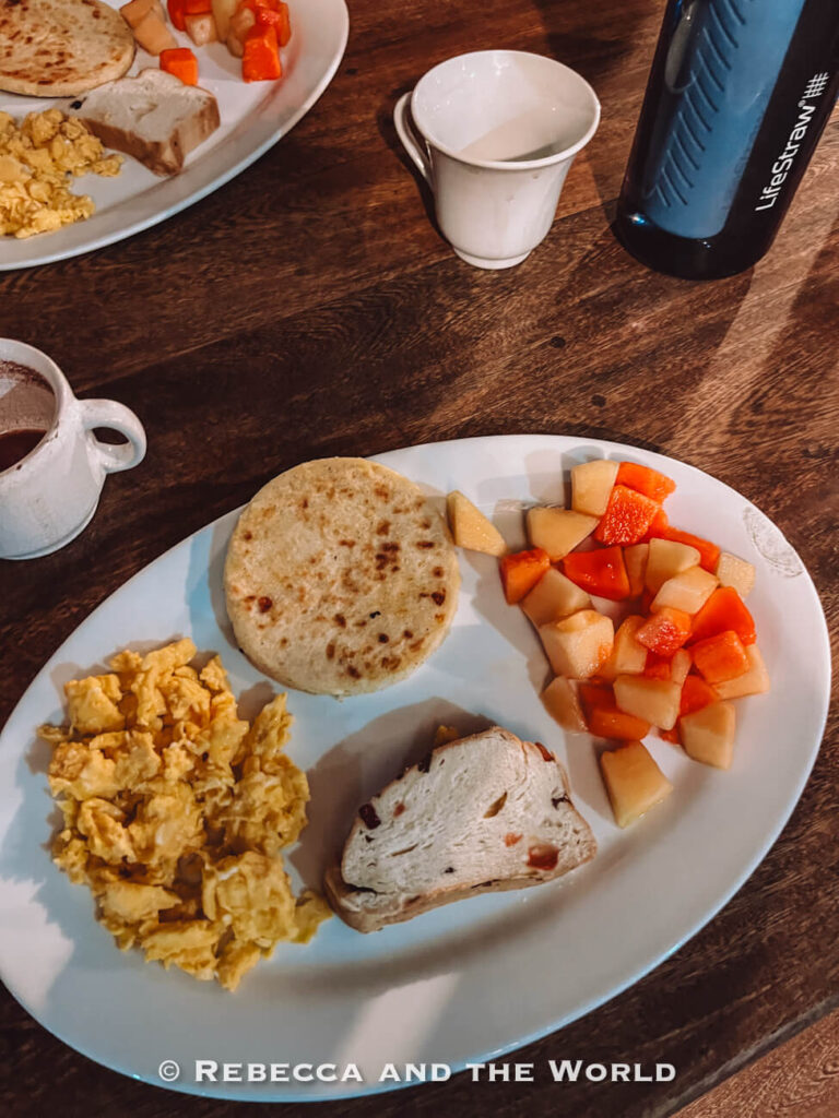 Simple breakfast plate with scrambled eggs, arepa, bread, and fresh fruit served before a day of hiking on the Ciudad Perdida trek.