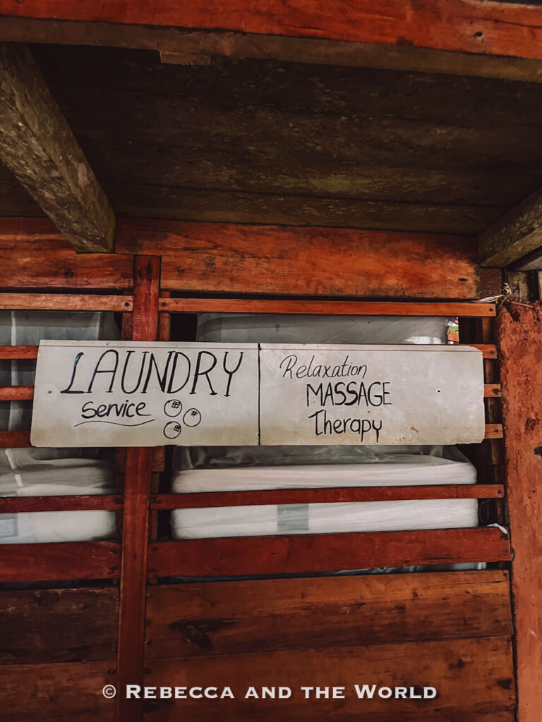 Handwritten wooden signs advertising laundry service and relaxation massage therapy inside a rustic jungle trekking camp.
