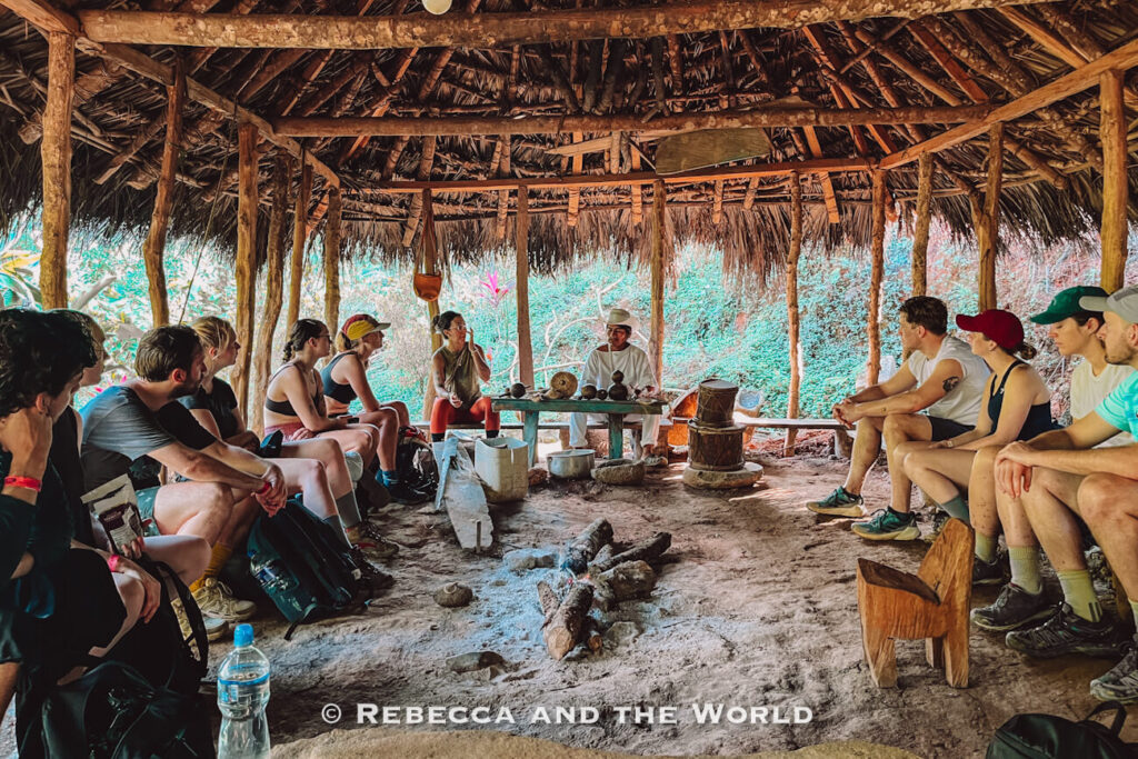 Group of trekkers sitting inside a circular thatched hut listening to an Indigenous guide speak during the Lost City trek.
