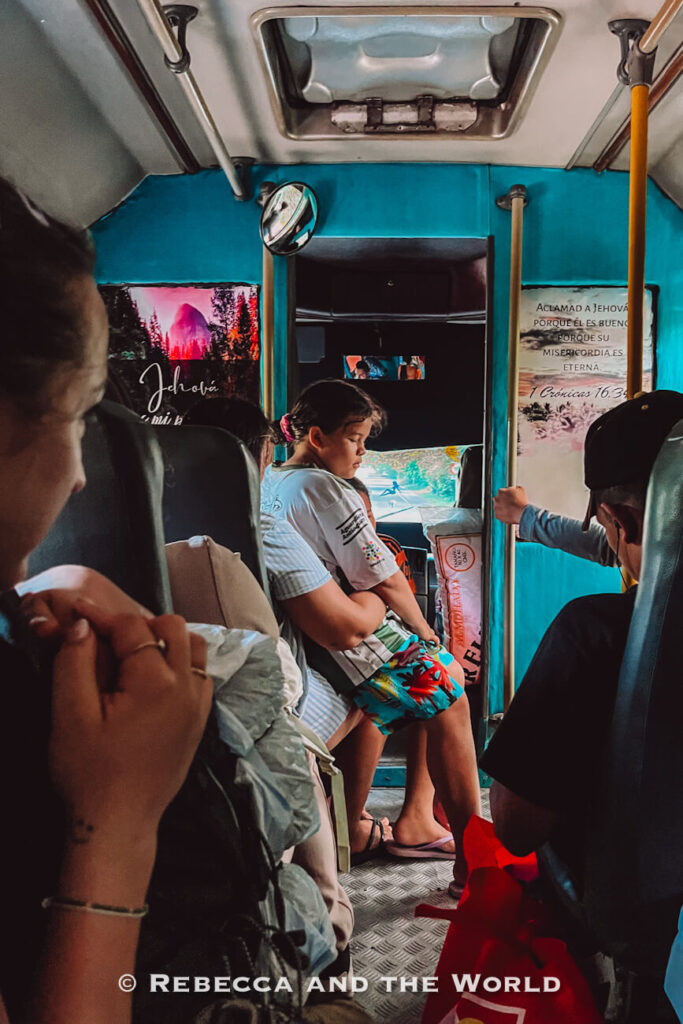 Passengers sit and stand inside a brightly painted bus with turquoise walls and religious decorations. The scene captures everyday transportation and local life, an experience many travelers encounter while exploring what to do in Palomino and the surrounding region.