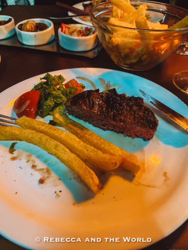 A partially eaten steak with fries and salad on a white plate, capturing a casual dinner experience while enjoying steak in Buenos Aires at Calden del Soho.