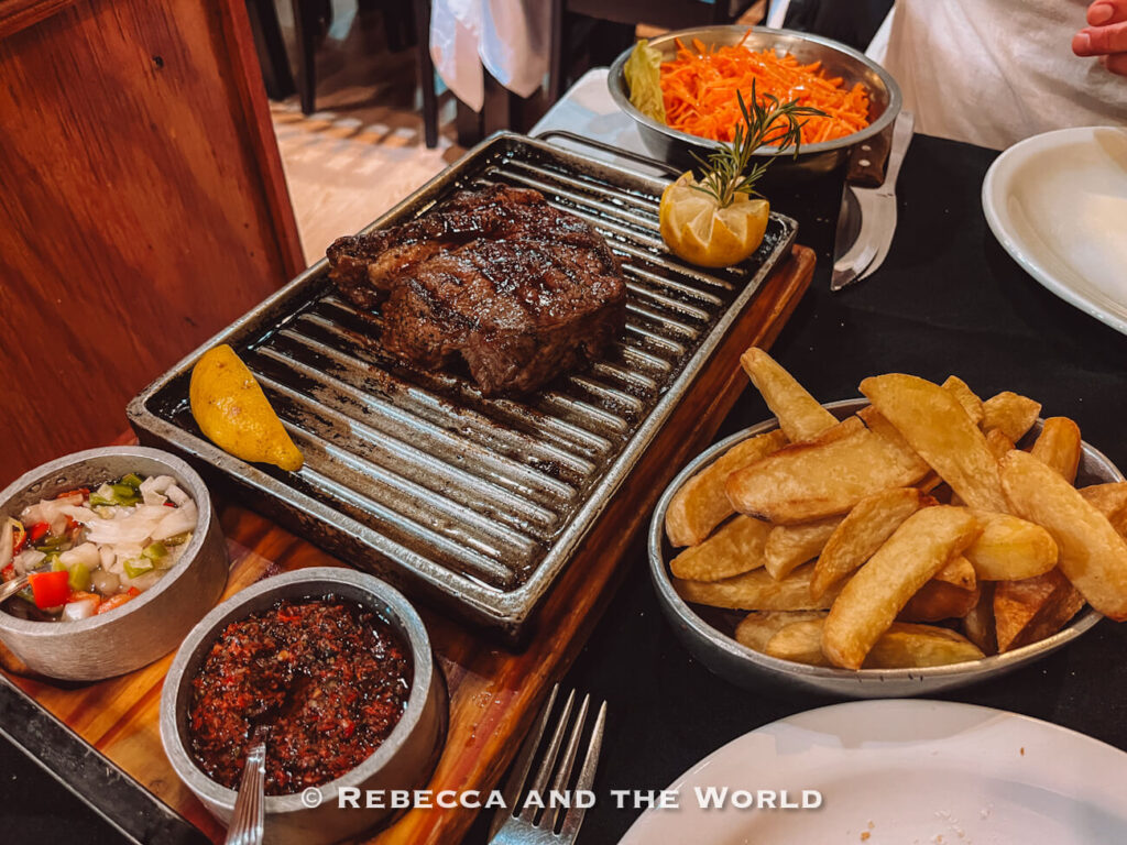 A thick grilled steak served on a sizzling metal parrilla with chimichurri, salad, and chunky fries at one of the best steak restaurants in Buenos Aires.