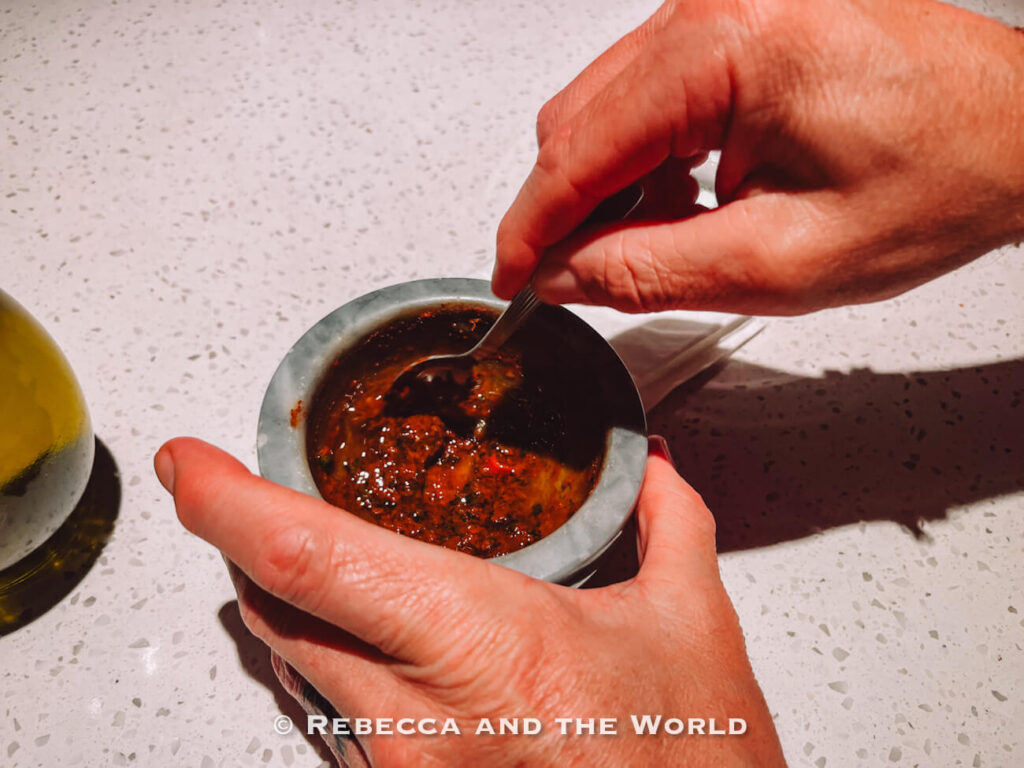 Hands stirring chimichurri sauce in a stone bowl on a restaurant counter during a cooking and dining experience in Buenos Aires.
