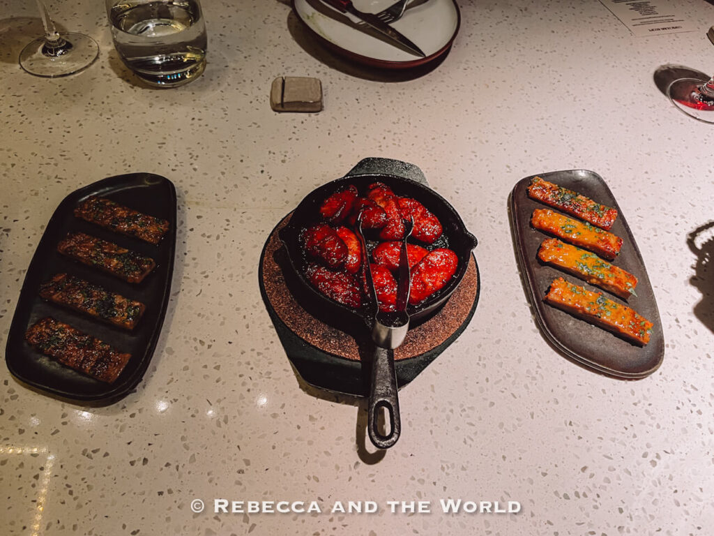 Assorted grilled side dishes served at The Argentine Experience, including sausages and pork arranged on black serving plates.