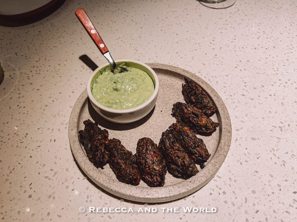 Charred grilled vegetables arranged around a bowl of creamy green dipping sauce on a ceramic plate at The Argentine Experience in Buenos Aires.