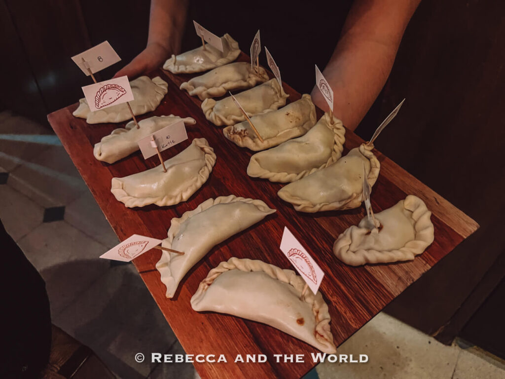 Wooden tray filled with uncooked empanadas labeled with small flags during an empanada-making activity at The Argentine Experience, one of the interactive things to do in Buenos Aires.