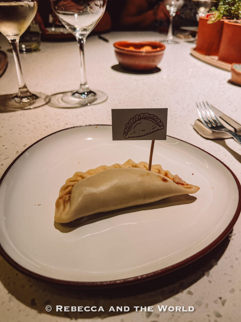 An empanada served on a white plate with wine glasses in the background at The Argentine Experience in Buenos Aires.