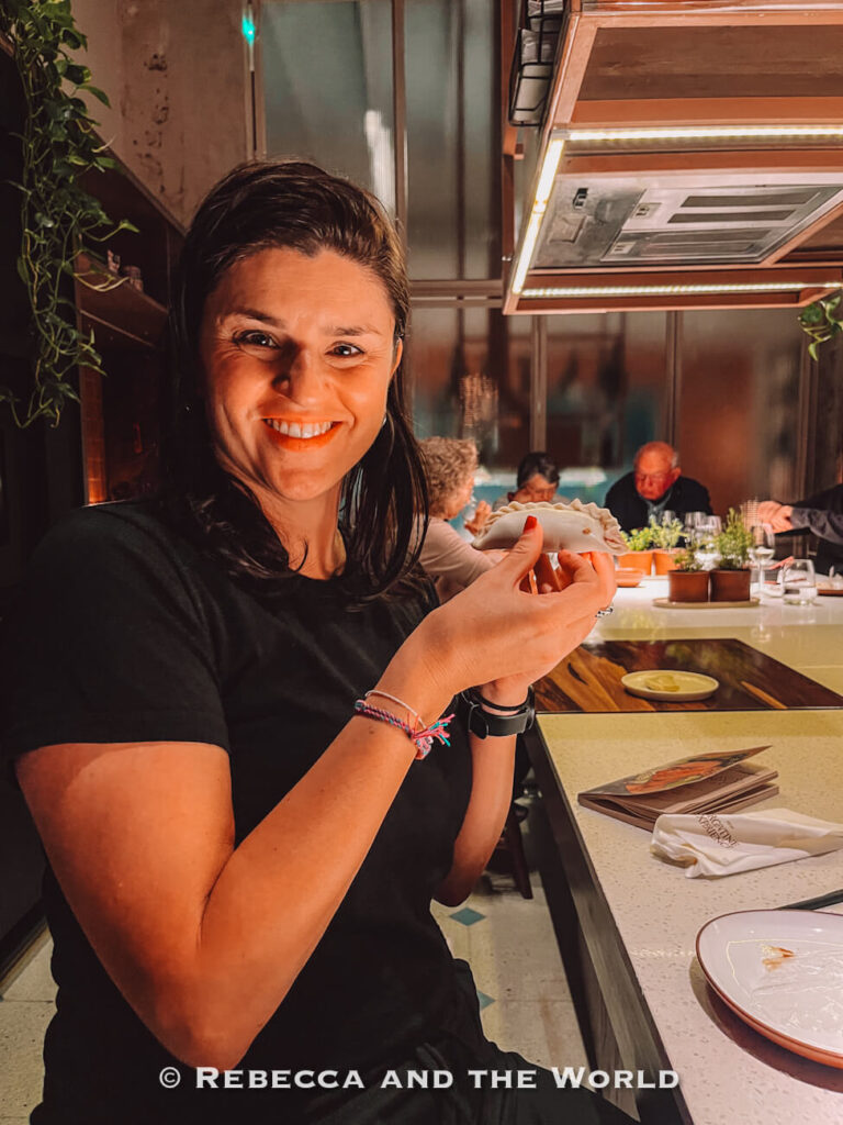 Woman (the author of this article) smiling while holding a handmade empanada at The Argentine Experience cooking class and dinner experience, a fun option for what to do in Buenos Aires.