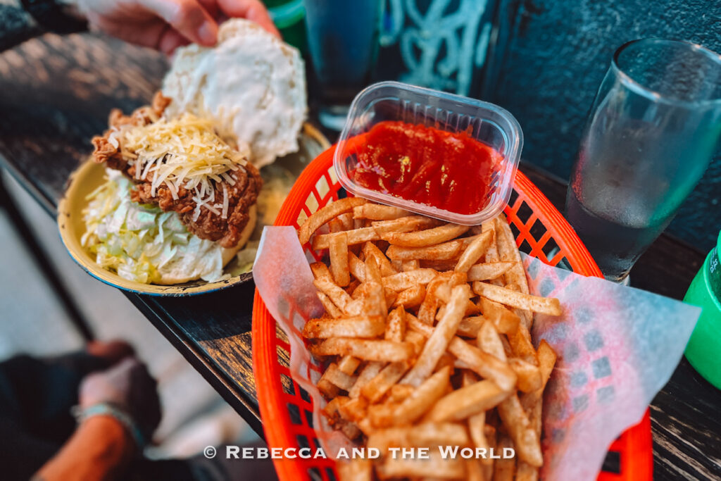Basket of crispy French fries served beside a fried chicken sandwich topped with shredded cheese and lettuce. Small containers of ketchup and drinks sit on the table, showing casual comfort food at Buenos Aires restaurants.