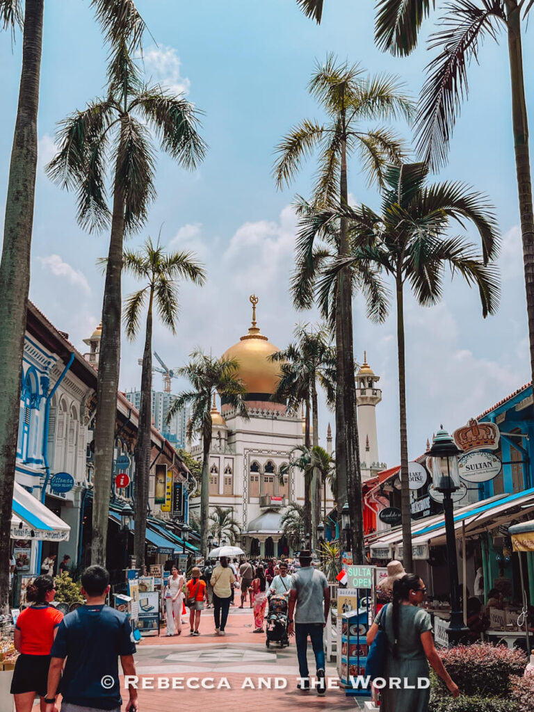 Palm-lined Bussorah Street crowded with pedestrians, shops and restaurants, with the golden dome of Sultan Mosque rising above Kampong Glam.