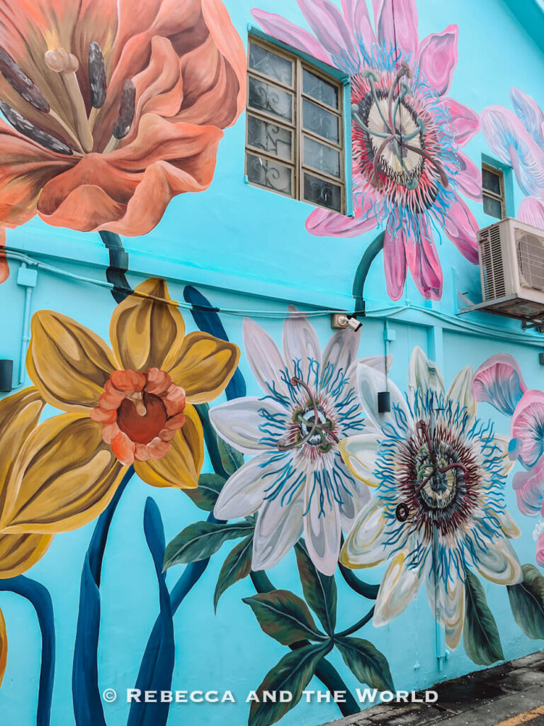 Large orange, yellow, white and pink flowers painted across a bright turquoise wall in Kampong Glam, one of the colourful things to do in Singapore.