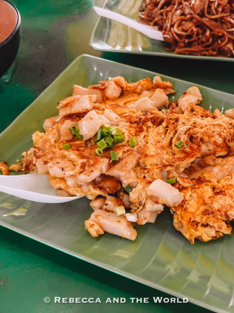 Singaporean chai tow kway, or fried carrot cake, made with cubes of radish cake, egg and spring onion, with noodles visible in the background.