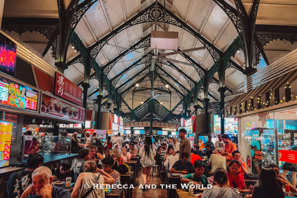 Crowds dining among brightly lit food stalls beneath the ornate cast-iron arches of Lau Pa Sat hawker centre, a popular stop during 2 days in Singapore.