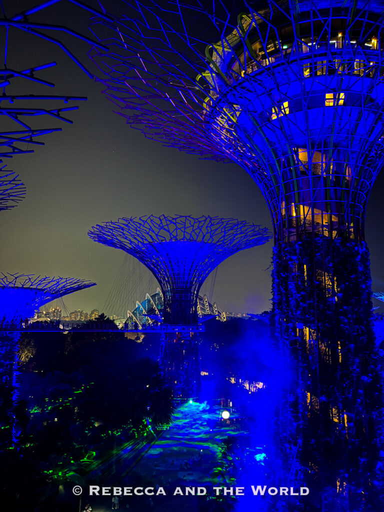 Supertree Grove glowing deep blue during the Garden Rhapsody light show, with mist and coloured lights illuminating the gardens below.