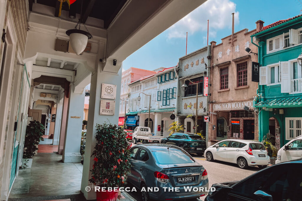 Traditional shophouses and historic Chinese clan buildings lining a central Singapore street, viewed from beneath a shaded five-foot way.