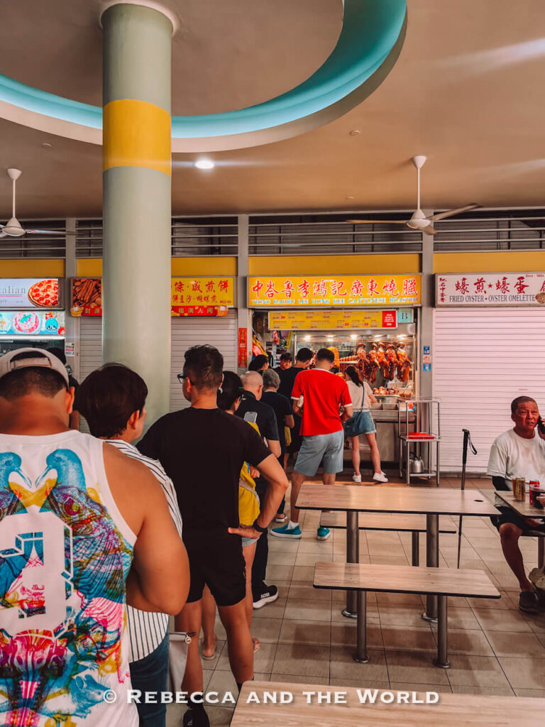 Long queue of customers waiting at Tiong Bahru Lee Hong Kee Cantonese Roasted, with roast ducks hanging in the hawker stall window.