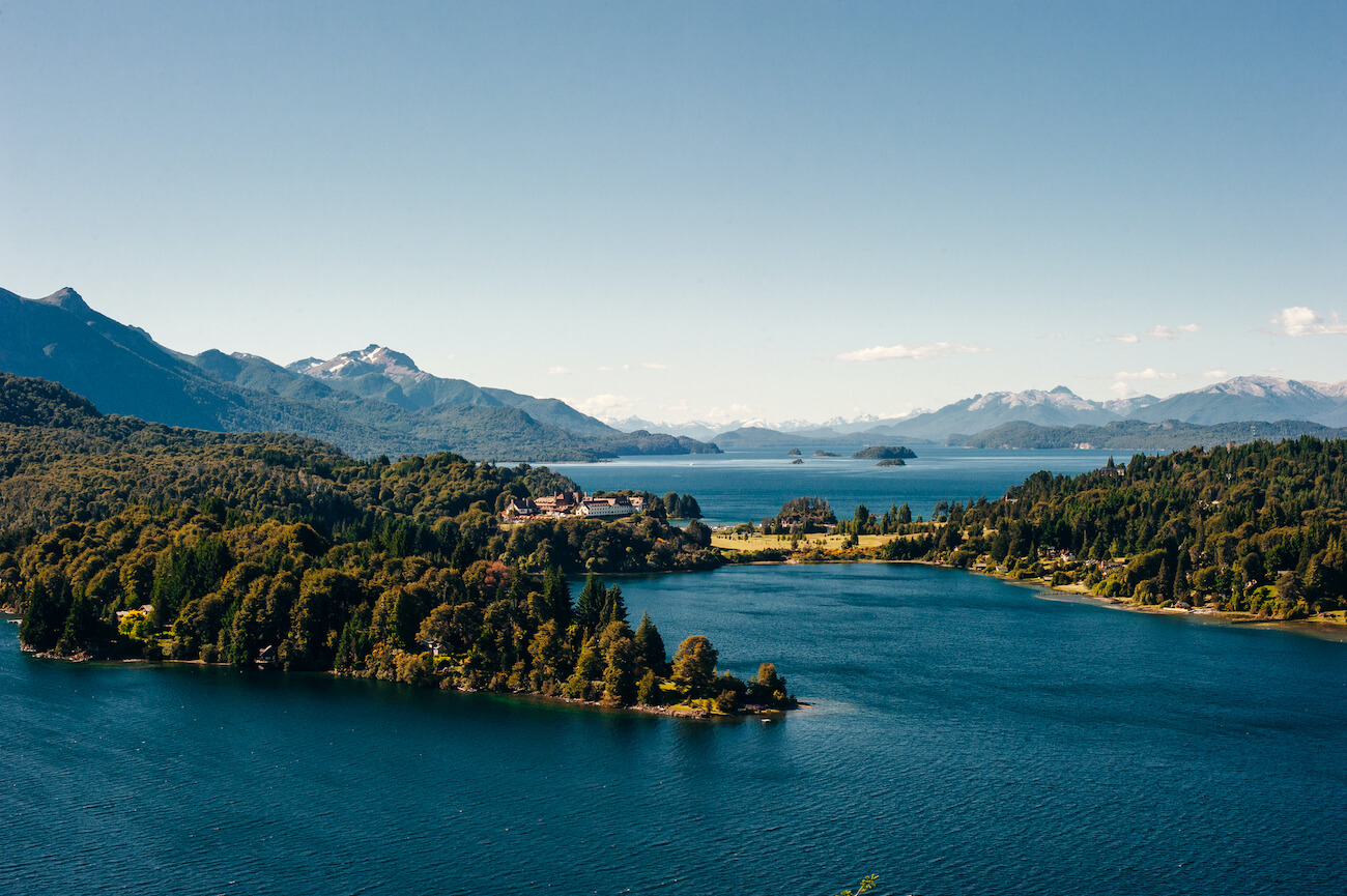 Panoramic view of Nahuel Huapi Lake near San Carlos de Bariloche, Argentina, showing forested islands, calm blue water, distant mountains, and a clear sky. Bariloche is one of the many places you can visit if you have 3 weeks in Argentina.
