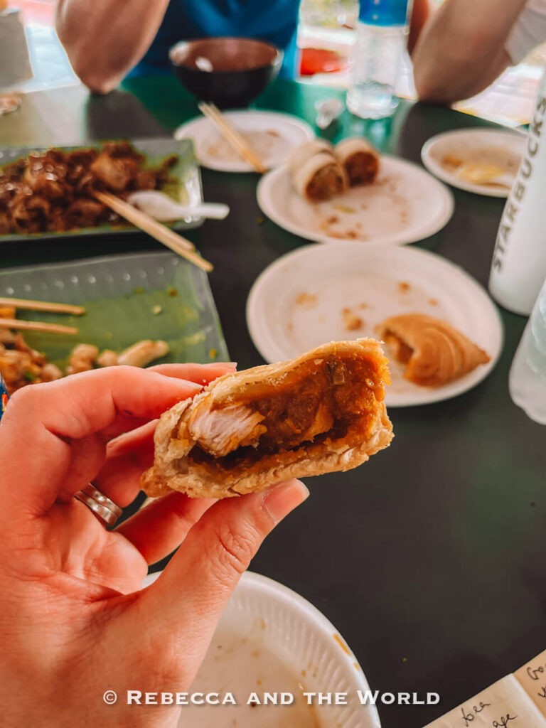 Close-up of a Singapore curry puff bitten open, showing the chicken, potato and curry filling