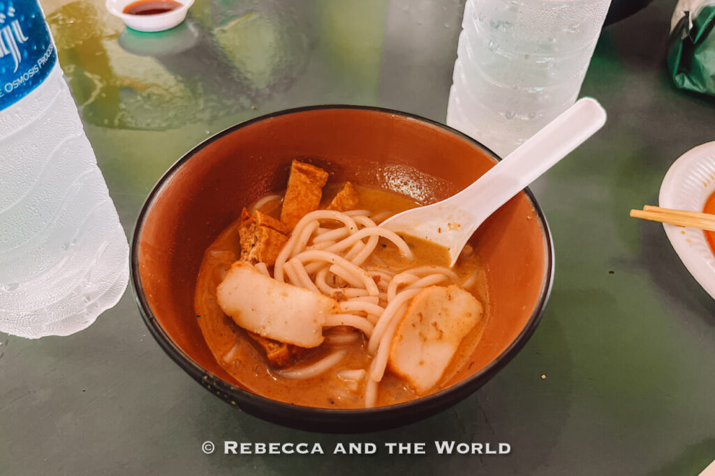 A bowl of Singapore laksa with tofu puffs and fish cake in a rich coconut curry broth