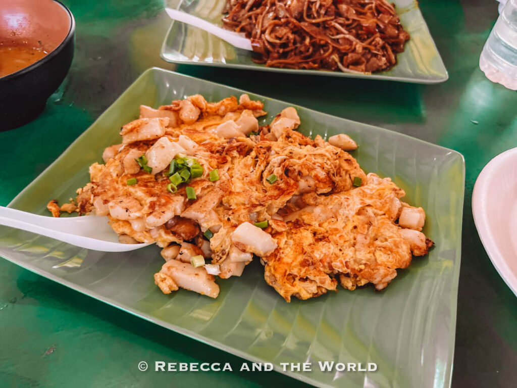 Singaporean chai tow kway, or fried carrot cake, made with cubes of radish cake, egg and spring onion, with noodles visible in the background.