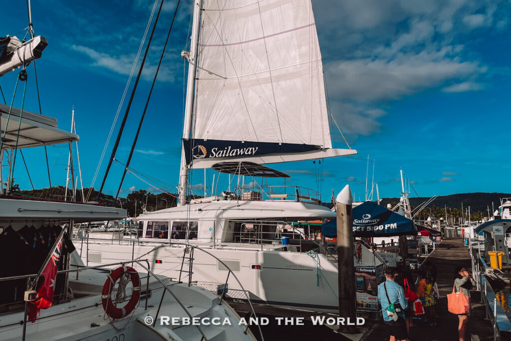 Sailaway catamaran with its branded white sail raised and passengers boarding at the Port Douglas marina dock ahead of a Great Barrier Reef day trip