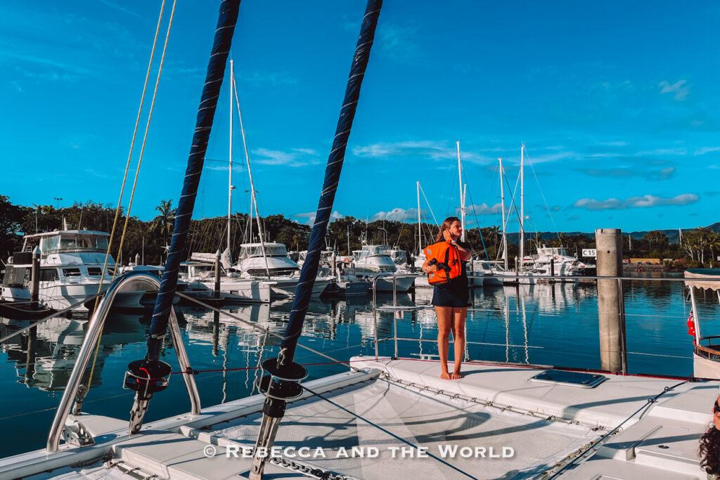 Crew member in an orange life jacket giving the pre-departure safety briefing on the bow of the Sailaway catamaran