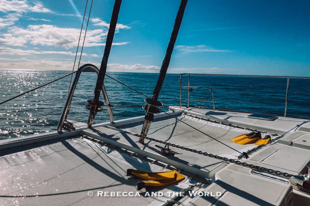 Netted trampoline deck at the bow of the Sailaway catamaran with yellow snorkelling flippers laid out, overlooking the open water on the way to the Great Barrier Reef