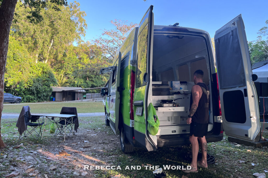Jucy campervan's rear kitchen set up at a shaded campsite in Cape Tribulation, with camping chairs and a table nearby