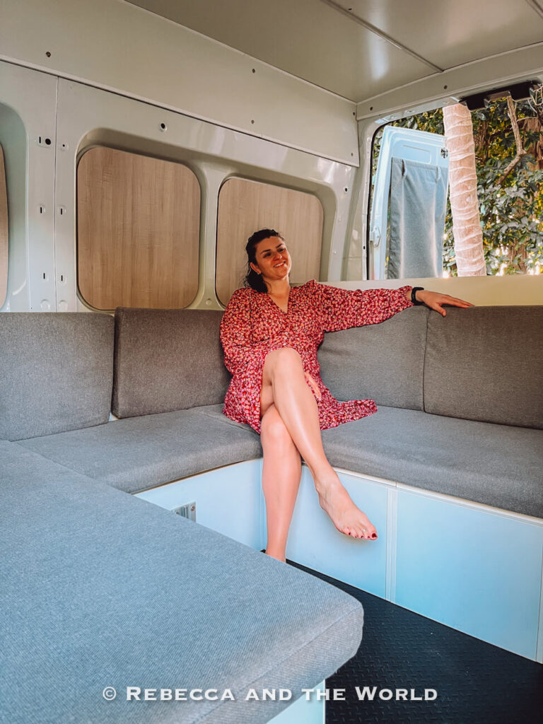 Woman (the author of this article) sitting on the interior bench seating of a Jucy campervan, showing the fold-down dining and lounge setup