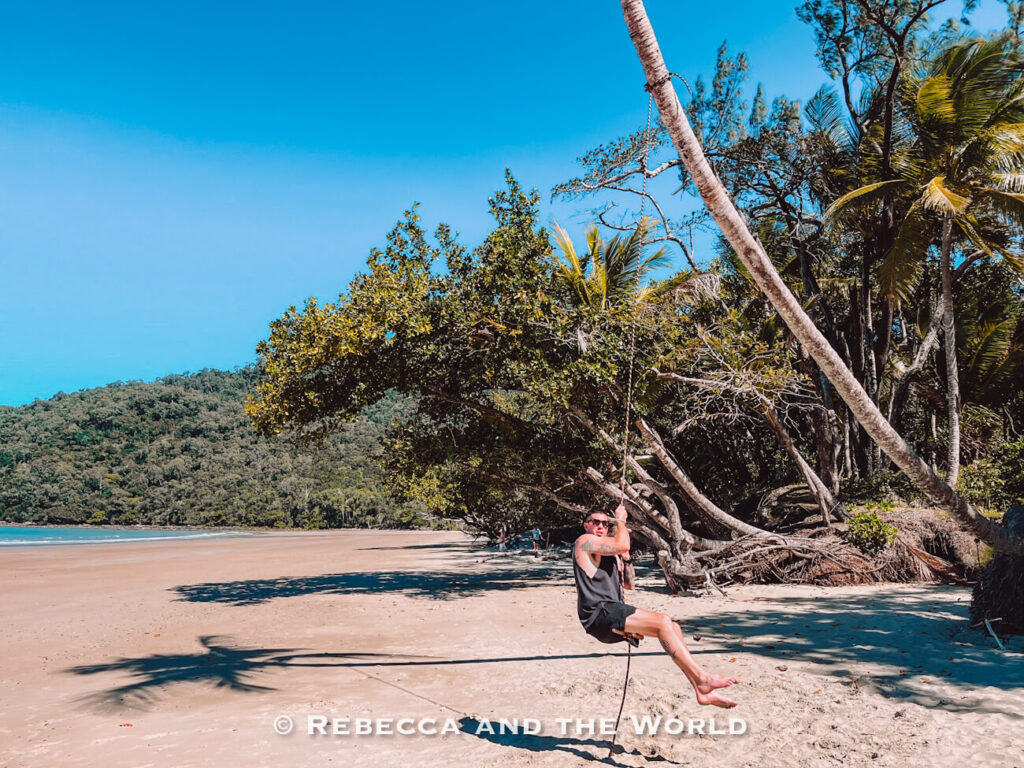 Rope swing hanging from a tree at Cow Bay beach near Cape Tribulation, with a man (the author’s husband) swinging on it