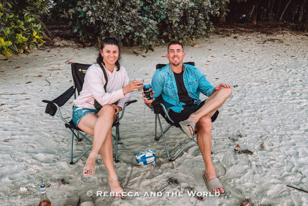 A man and a woman (the author and her husband) Sitting down with drinks on the sand at Cape Tribulation Beach at the end of the day