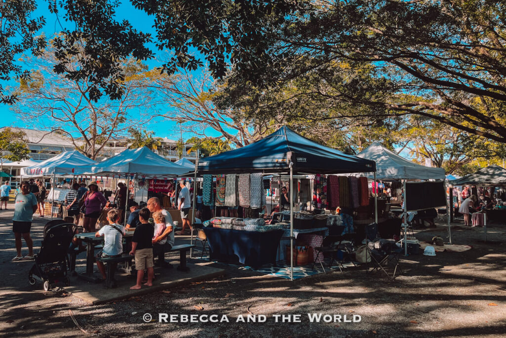 Stallholders and shoppers browsing the Port Douglas Sunday markets under shaded trees