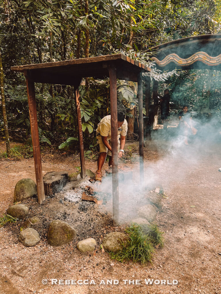 A Kuku Yalanji guide tends a smoking fire under a timber shelter at the start of the Ngadiku Dreamtime Walk, one of the best things to do in Mossman Gorge