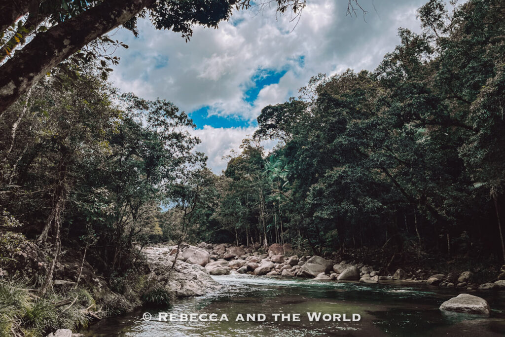 The boulder-strewn Mossman River under a blue sky with rainforest on both banks, seen from the Lower River Track at Mossman Gorge