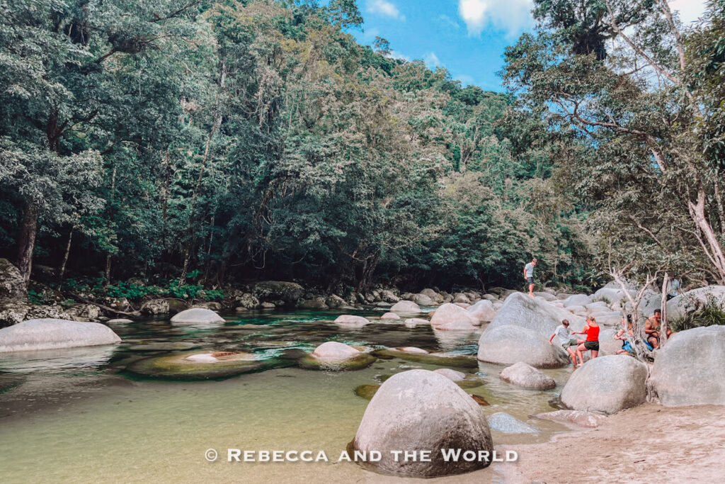 Visitors sitting on smooth granite boulders beside the clear green water of the Mossman River, the most popular Mossman Gorge swimming spot