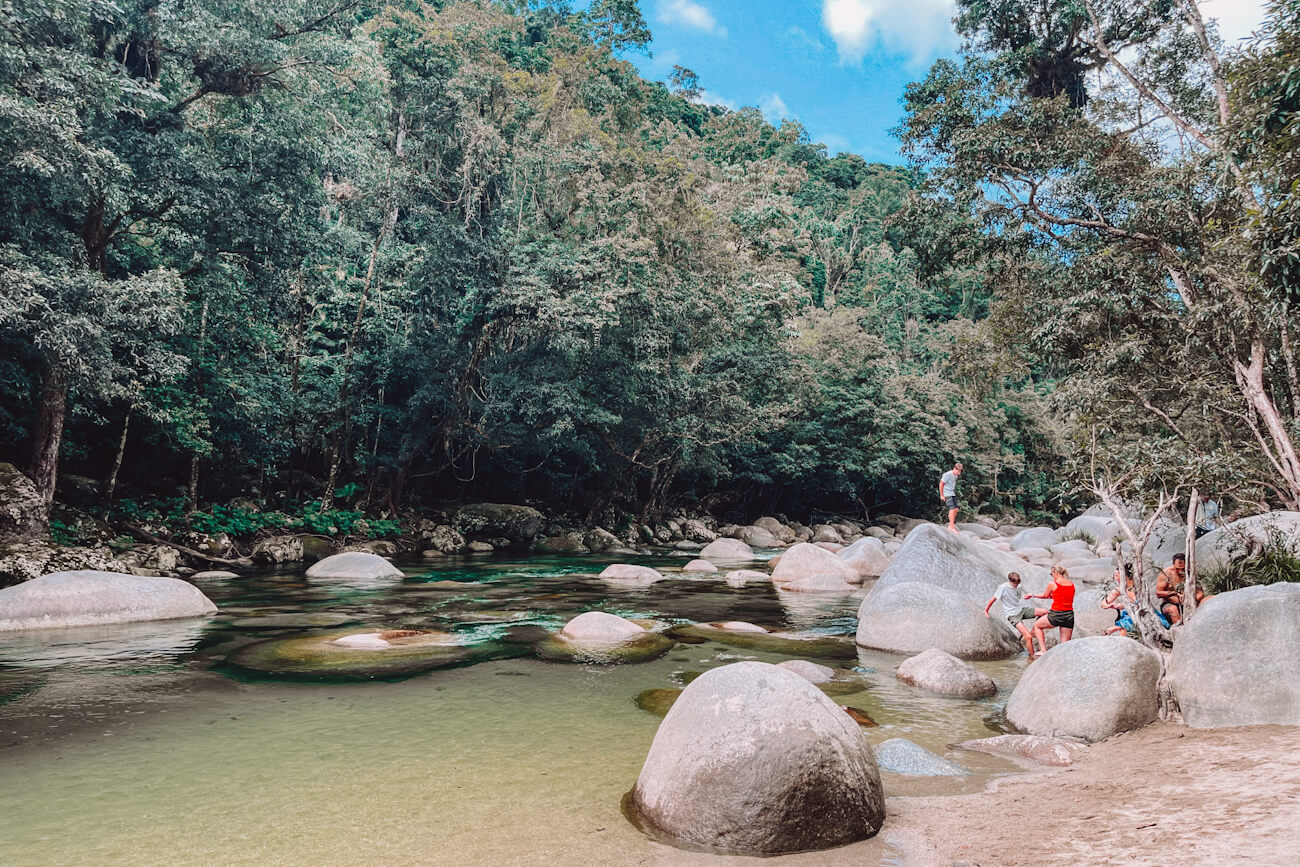 Visitors sitting on smooth granite boulders beside the clear green water of the Mossman River, one of the best things to do in Mossman Gorge